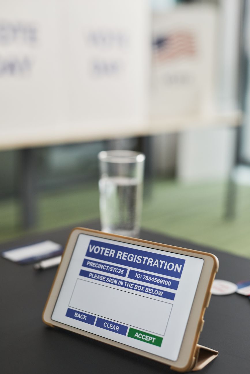 Tablet showing digital voter registration check-in at a polling place, illustrating the administrative burden of cross-checking voter records.