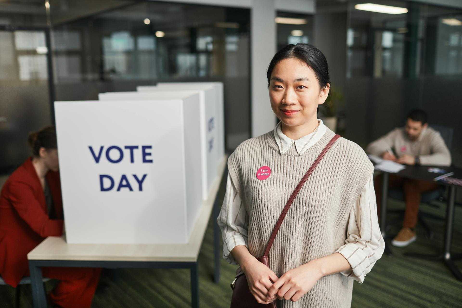 Asian woman at voting booth on Election Day, proudly displaying 'I am a voter' sticker.