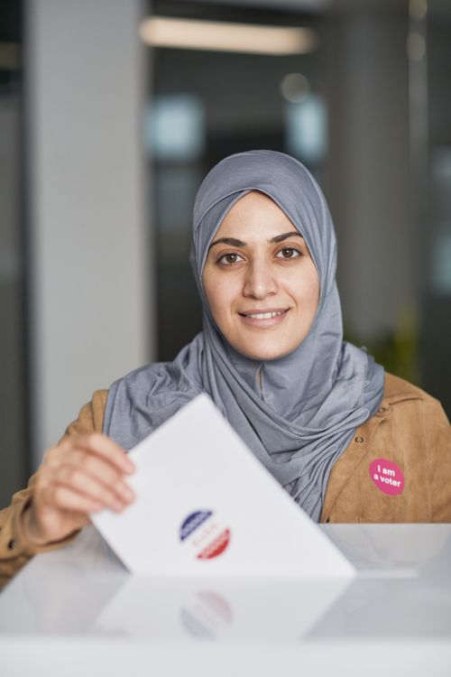 Free Smiling woman in hijab casting her vote during election day indoors. Stock Photo
