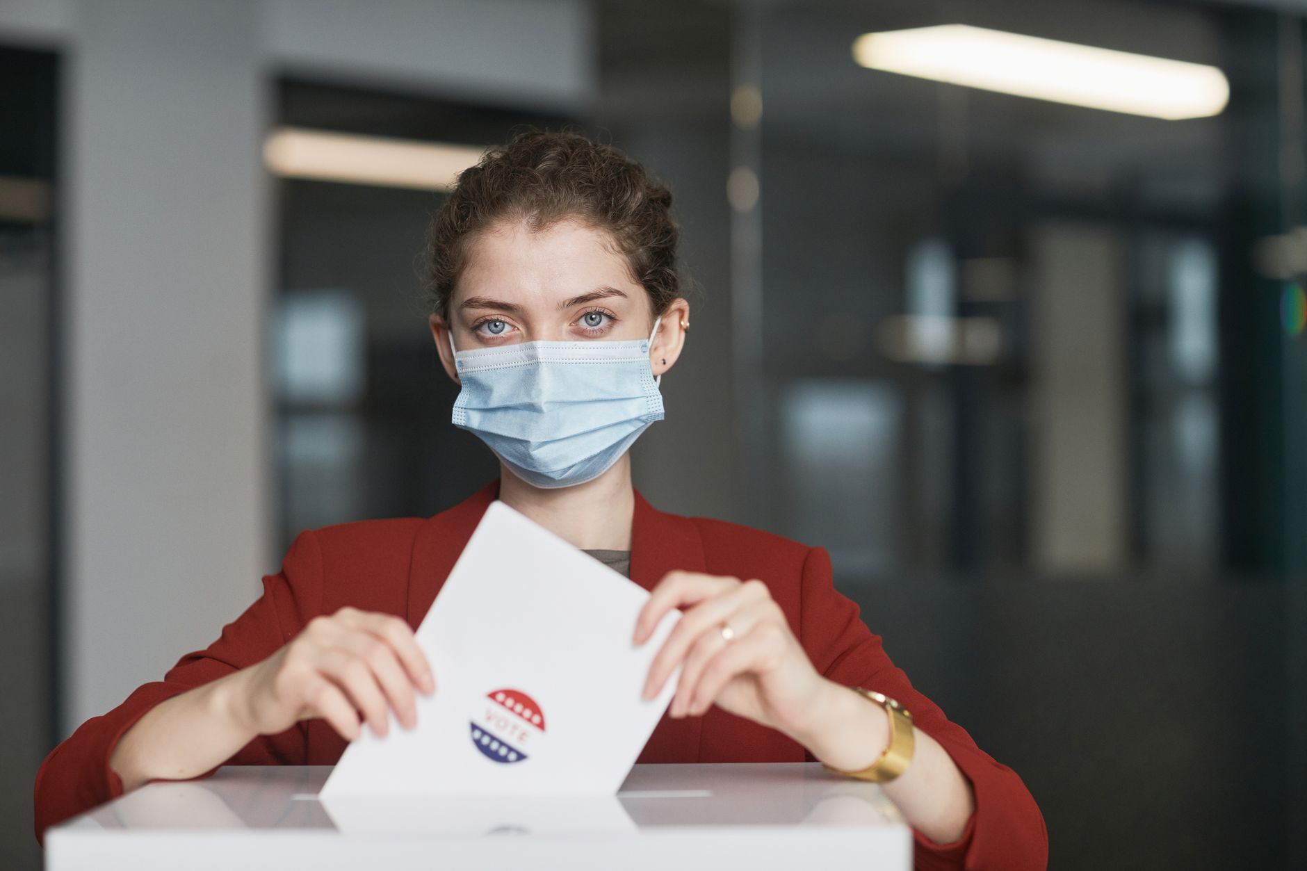 A woman wearing a face mask places a ballot in the box on election day with safety measures.