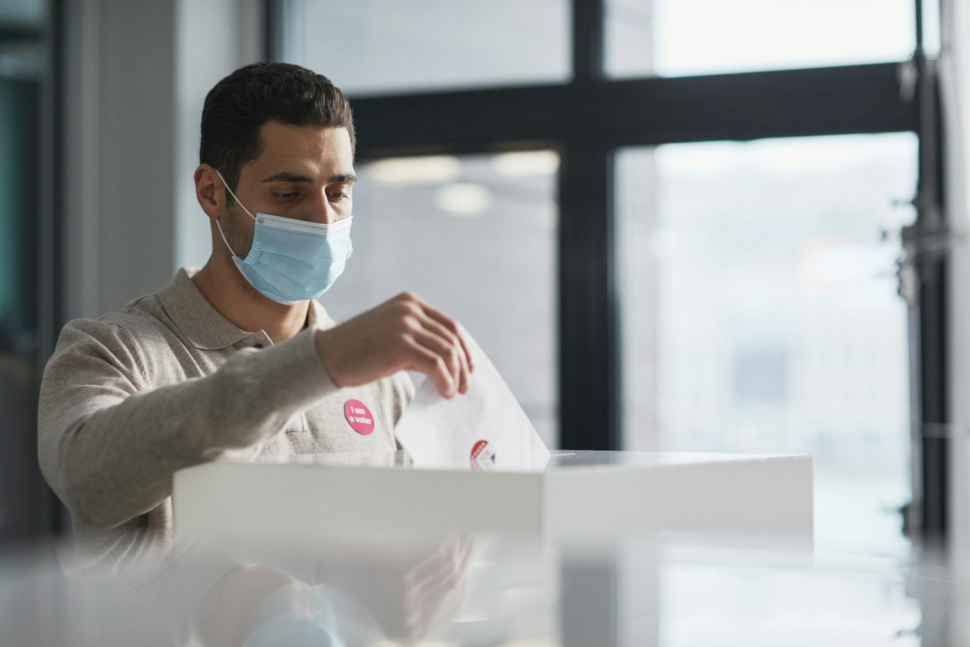 Man wearing a face mask casting his vote indoors during pandemic.