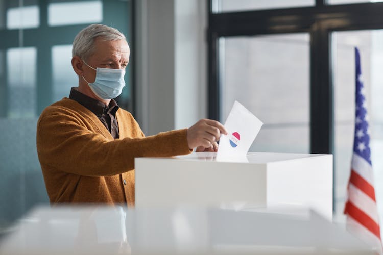 An Elderly Man Dropping A Paper In A Ballot Box