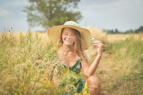 A Woman in Printed Dress and Straw Hat Collecting Grass Flowers