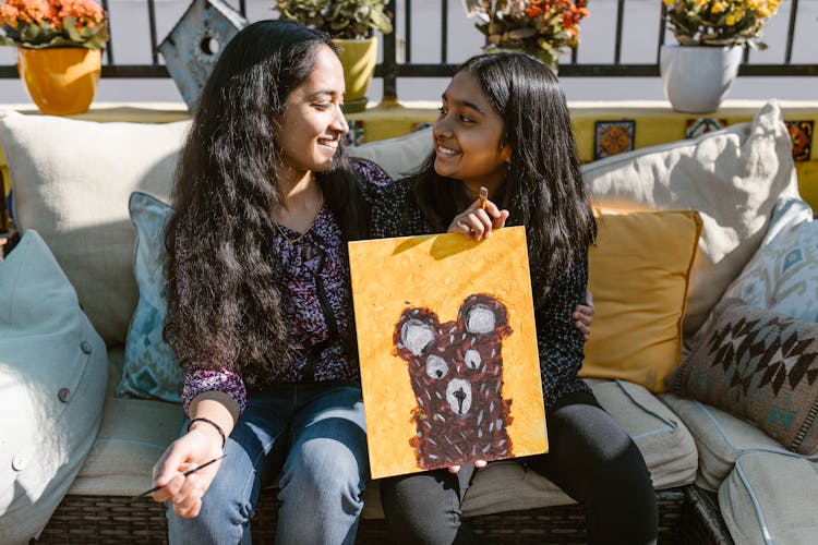 A Woman And Girl Smiling At Each Other While Holding A Painting