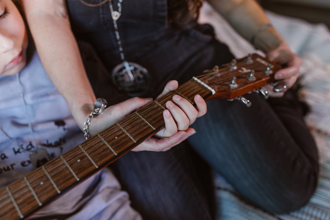 Free Anonymous young mother with little son practicing on guitar at home Stock Photo