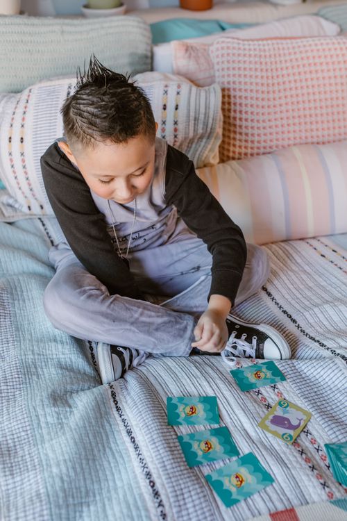 Free From above of cute preteen boy in casual clothes with stylish haircut sitting on comfortable bed with crossed legs and playing card game Stock Photo
