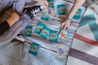 Top view of crop anonymous kid with mother playing card game with colorful marine pictures on bed during weekend at home