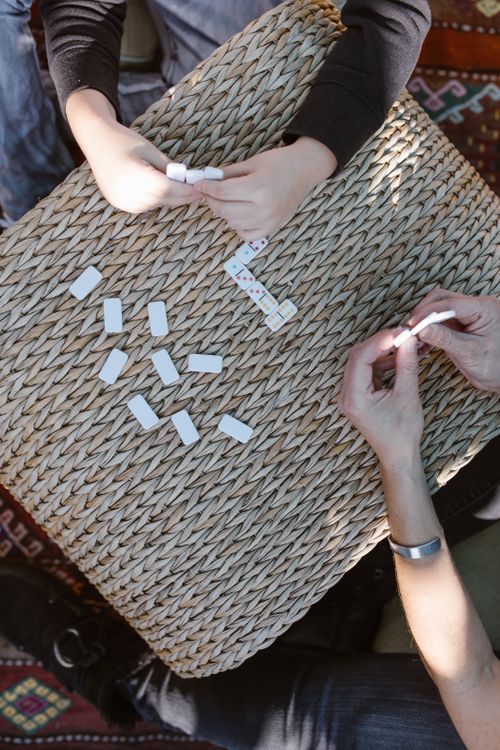 Free Hands of multiple people playing dominoes on a woven table, captured from above for a casual game setting. Stock Photo