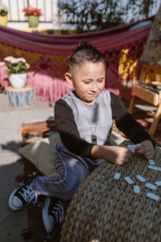 A young boy enjoying a game of dominoes outside, surrounded by colorful decor, in the sunlight.