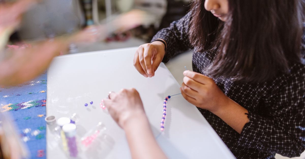 Un enfant créant des bracelets en perles de manière créative à l'intérieur, concentré sur l'activité artistique et artisanale.
