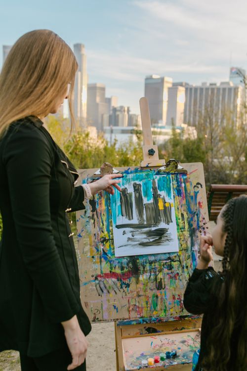 Free A woman and girl enjoy outdoor painting in a city park, surrounded by nature and skyscrapers. Stock Photo
