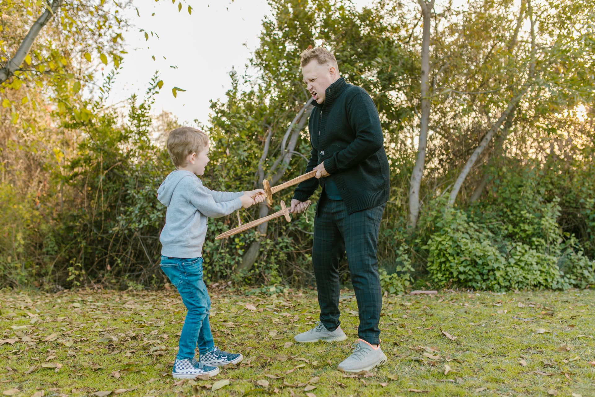 A playful bonding moment between a father and son playing with wooden swords in a grassy field.