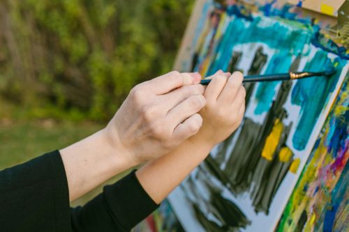 Free A close-up of a mother and child painting together on a canvas outdoors, fostering creativity. Stock Photo