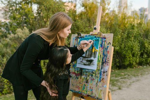 Free Mother guiding daughter in a painting session outdoors, bonding over art. Stock Photo