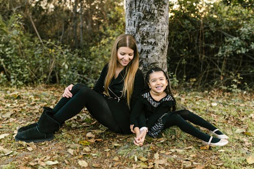 Free Woman and Her Child Sitting on the Ground under the Tree Stock Photo