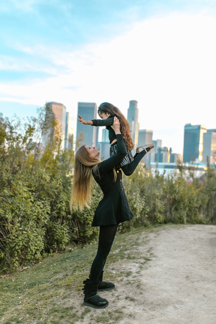 A Woman Holding Her Daughter In The Air At A Park