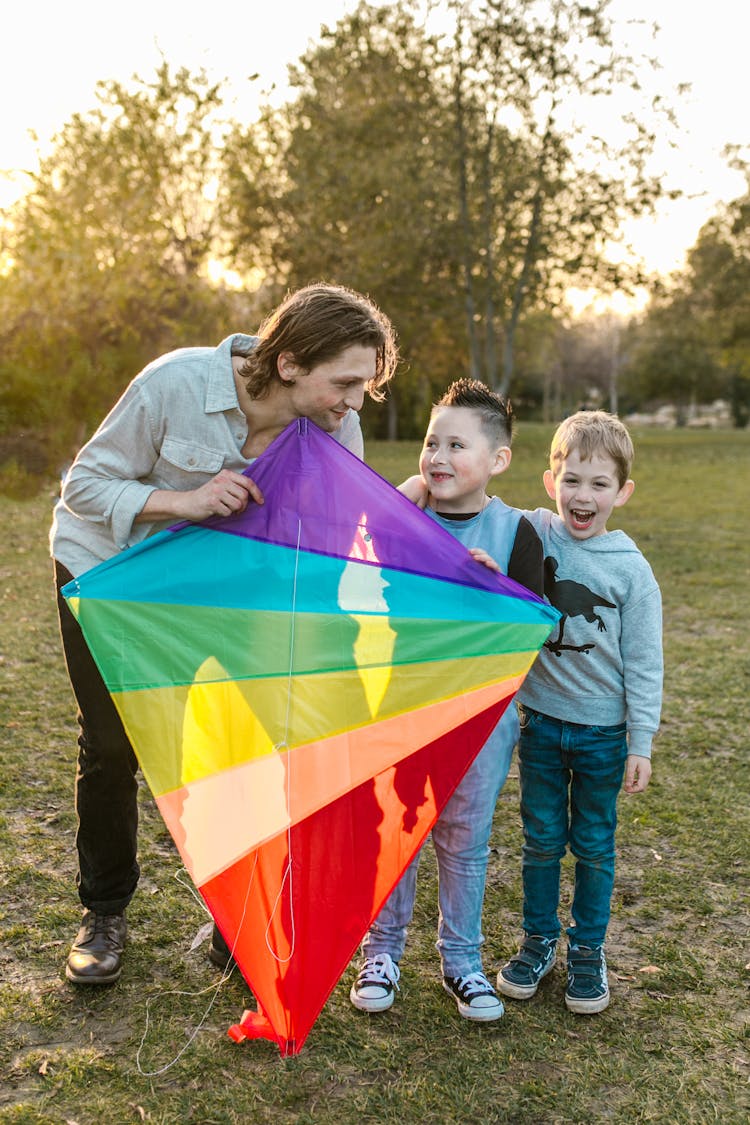 A Man Holding A Colorful Kite Standing Beside Two Boys