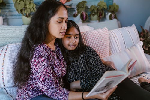 Mother and Daughter Reading a Book while Sitting on the Couch