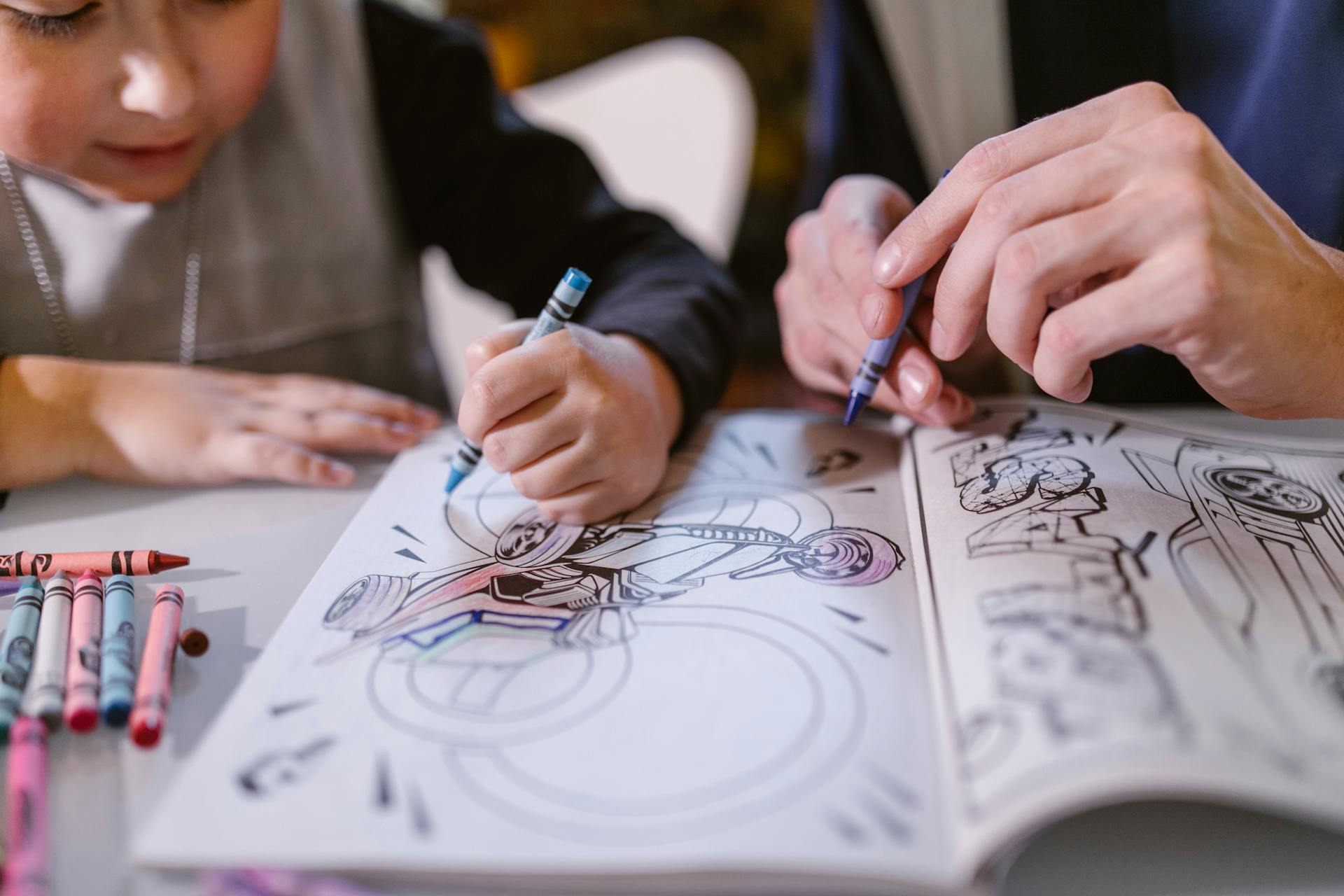 Child and an adult coloring a biker image in a coloring book, using crayons.