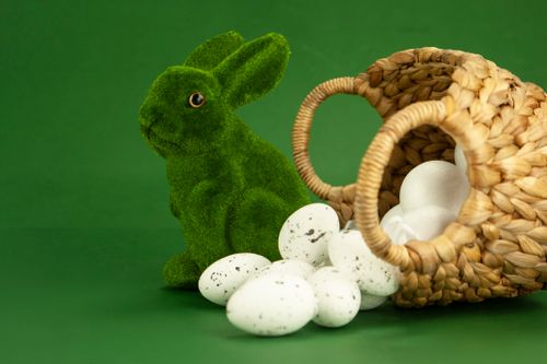 Free Green bunny figurine with quail eggs and woven basket on a green background. Stock Photo