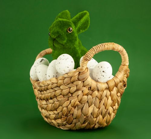 Free Festive Easter display with green bunny and speckled eggs in a woven basket on a green background. Stock Photo