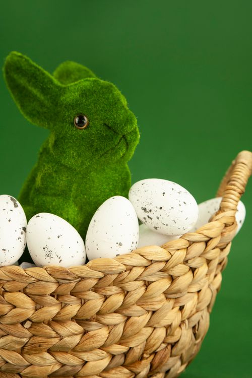 Free A whimsical green moss bunny sits among Easter eggs in a woven basket, set against a vibrant green background. Stock Photo
