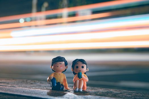 Cute figurines of boy and girl placed near asphalt road with long exposure light trails on street in evening time