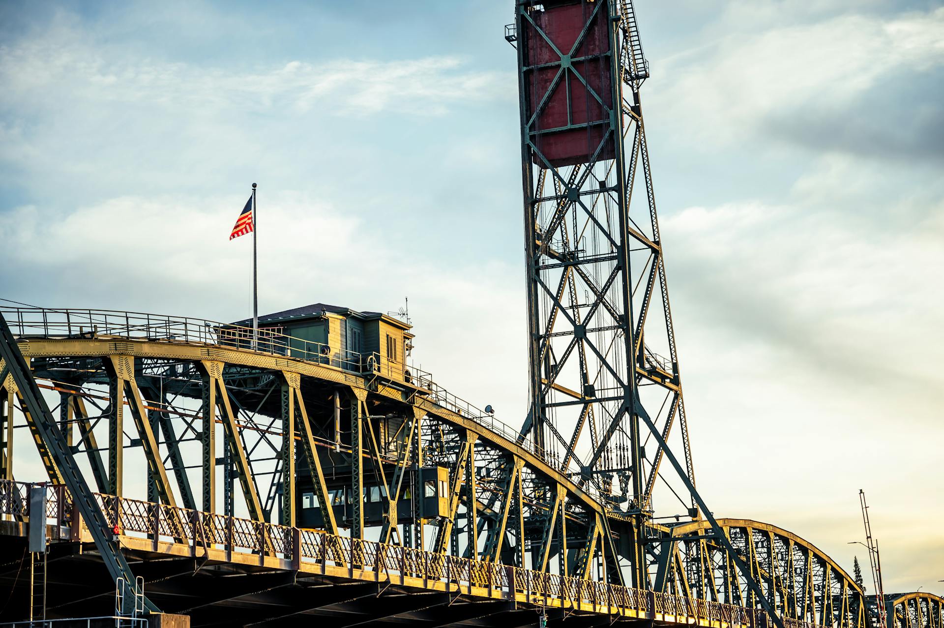 Low angle of metal Hawthorne Bridge with vertical lift and waving US flag against cloudy sunset sky in Portland