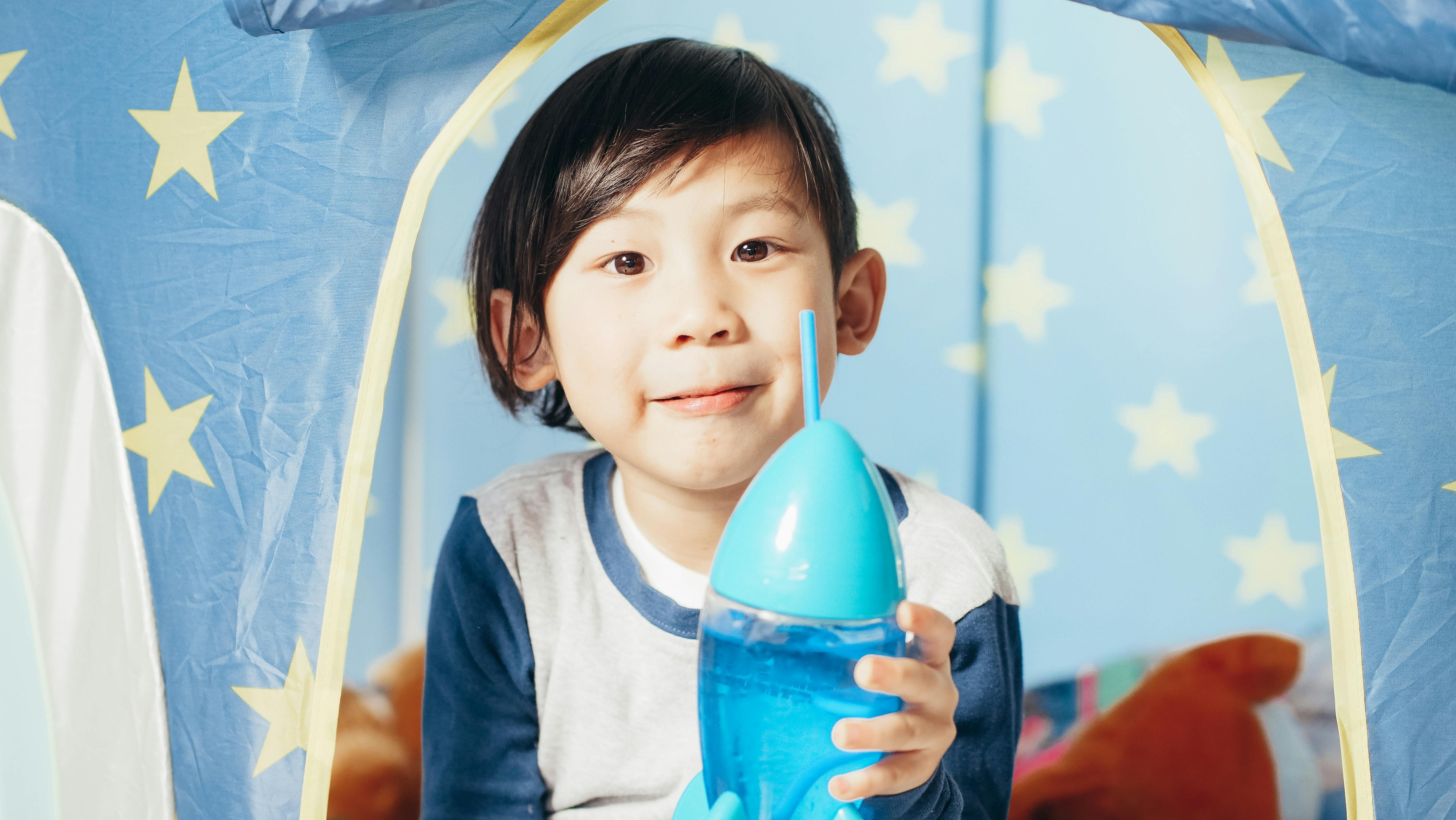 Young boy enjoying playtime inside a starry-themed tent while holding a toy rocket bottle.