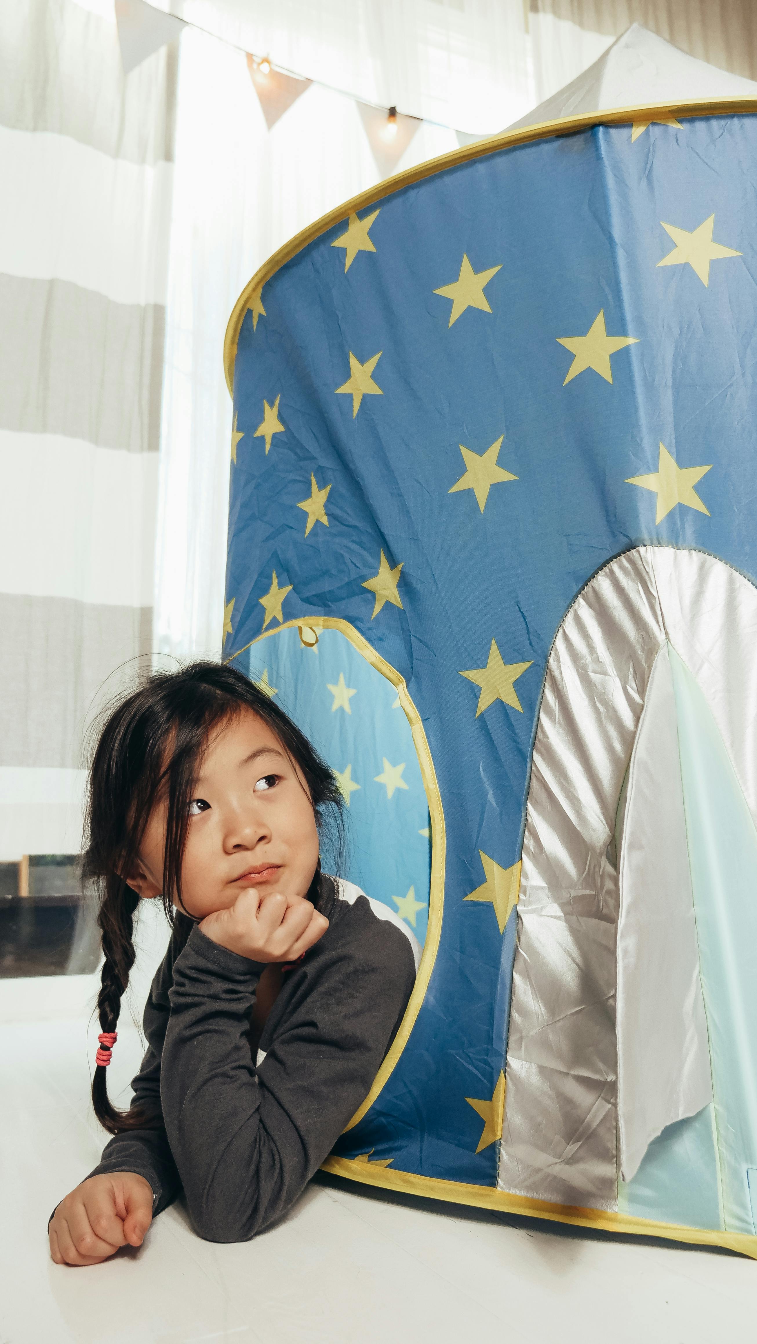 Free Young girl with braided hair playing in a starry themed indoor tent. Child's imaginative play session. Stock Photo