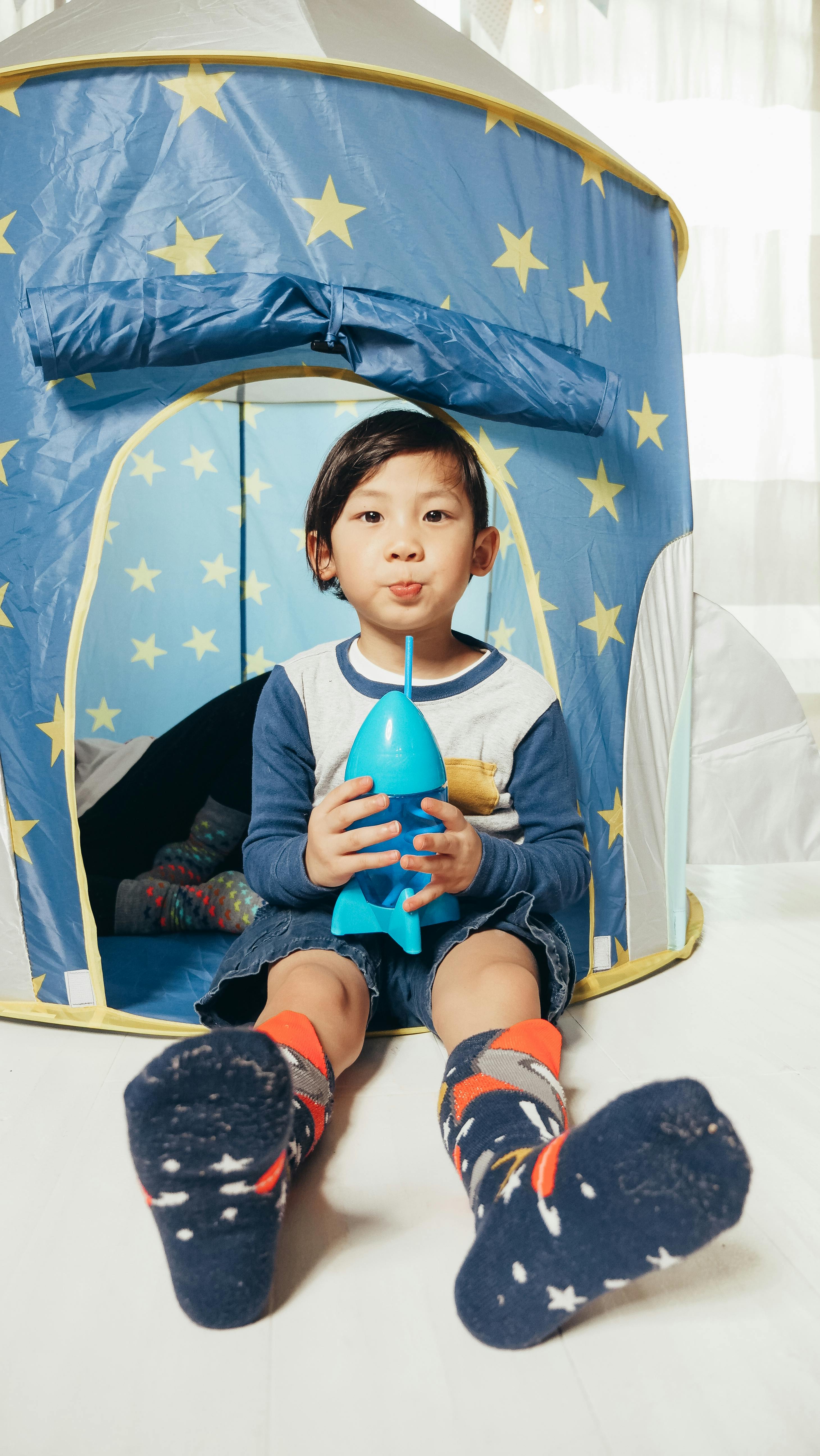 Free Cute Asian boy enjoying playtime in a star-themed indoor tent with a rocket toy. Stock Photo