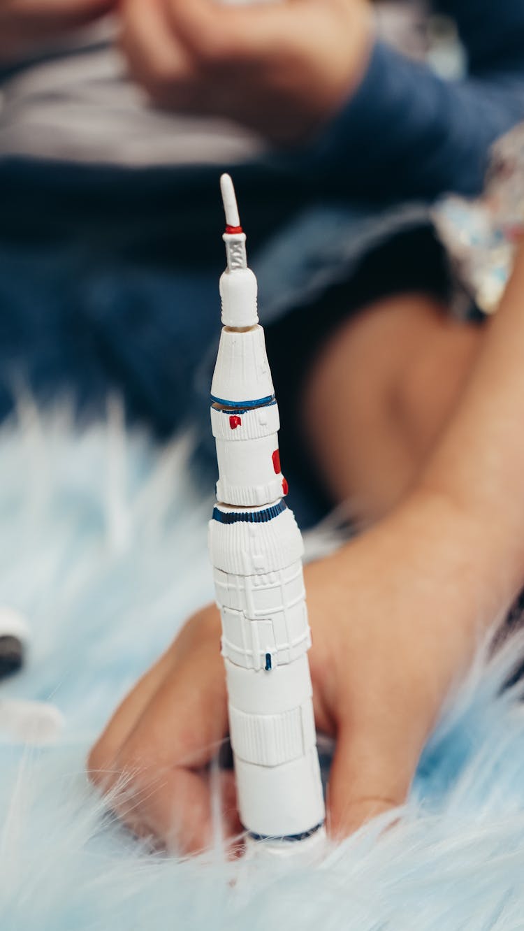 Hand Holding A Toy Rocket Ship On Rug