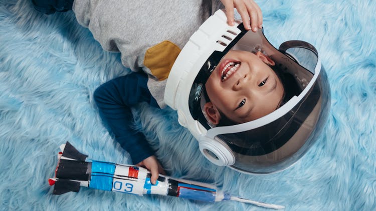 A Boy In An Astronaut Costume Holding A Rocket