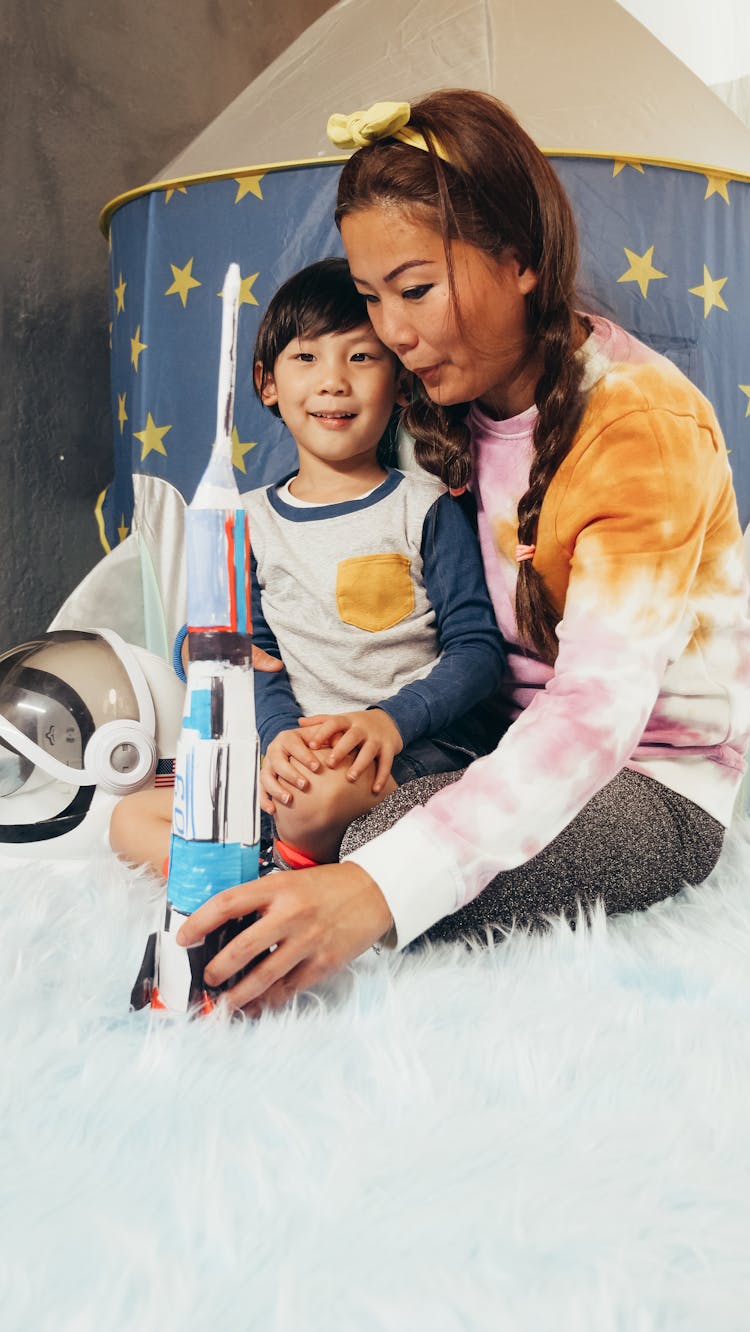 Child And Woman Holding A Toy Rocket Sitting On A Rug