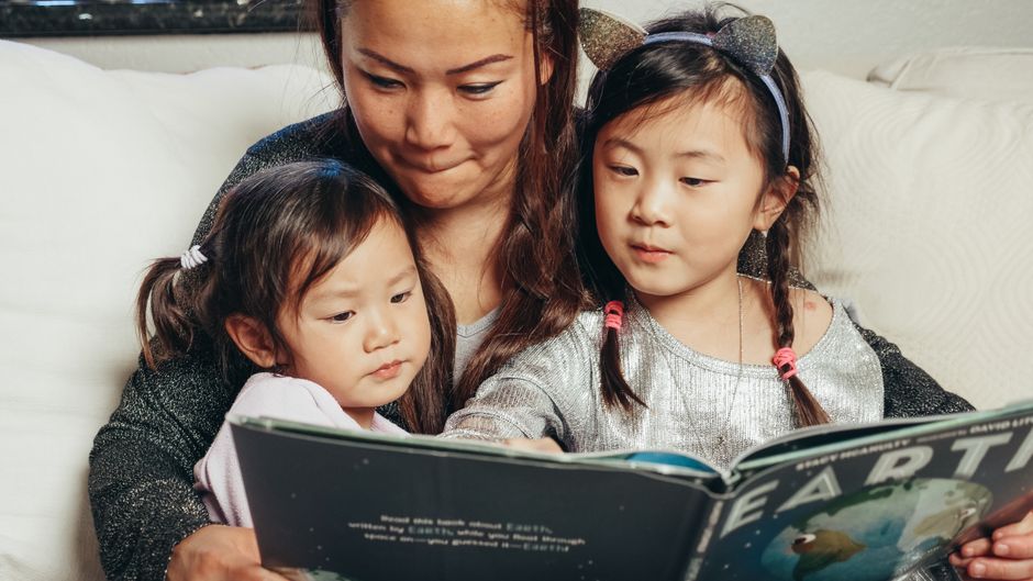 A mother and her two children reading a picture book together at home