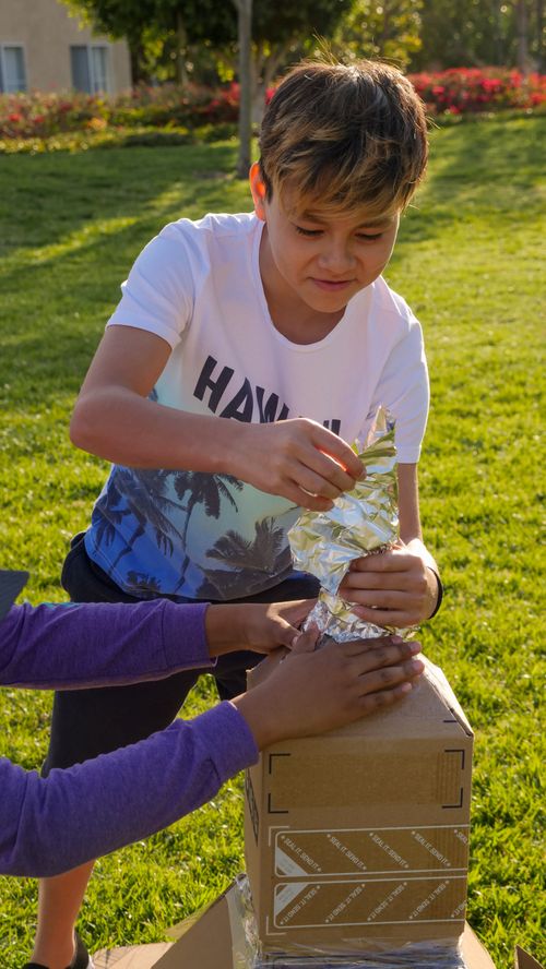 Free Two children enjoying a sunny day assembling a cardboard rocket in a park. Stock Photo