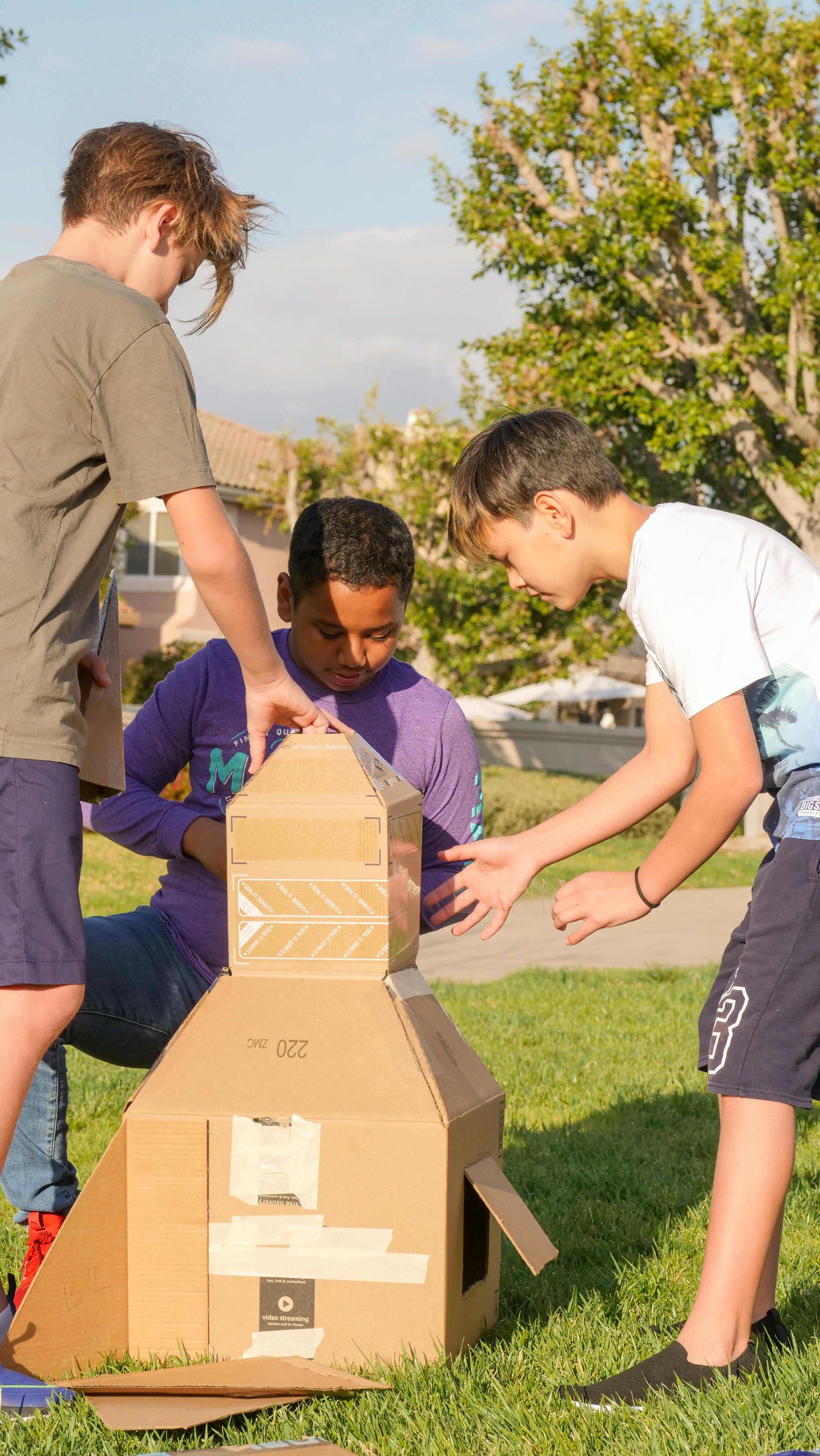 Children playing with a cardboard rocket in a sunny park, fostering teamwork and creativity.