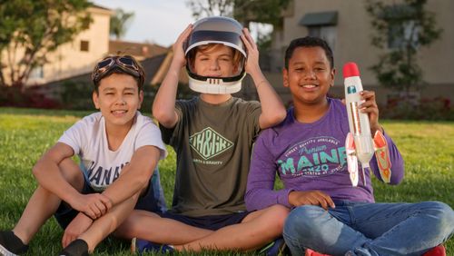 Free Three kids sitting on grass, playing with a toy rocket, enjoying a sunny day. Stock Photo