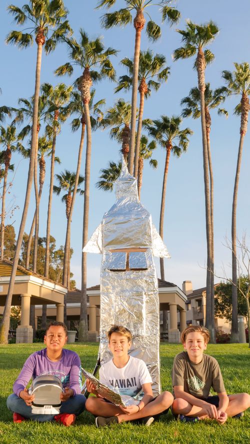 Free Three boys sit with a homemade cardboard rocket on a sunny day outdoors. Stock Photo