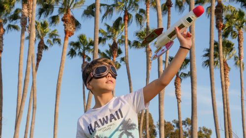 Free A child joyfully playing with a toy rocket under palm trees on a sunny day. Stock Photo
