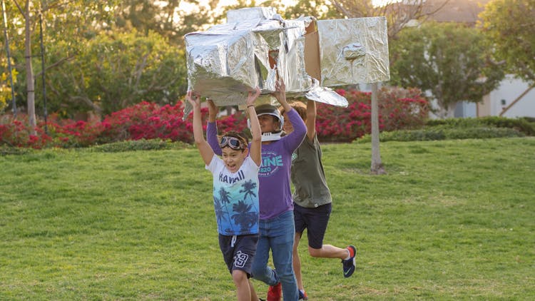 A Group Of Boys Running With A Silver Object 