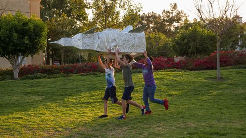 Free Three children enjoy outdoor playtime by crafting and carrying a cardboard rocket. Stock Photo