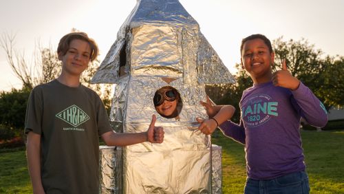 Free Three kids enjoy outdoor play with a handmade foil rocket on a sunny day. Stock Photo