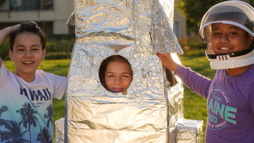 Free Three kids having fun with a cardboard rocket outdoors during the day. Stock Photo