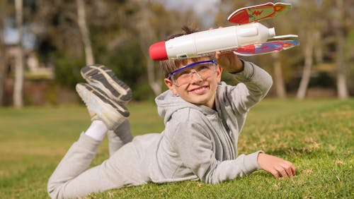 A Boy in Gray Jacket Playing a Rocket on a Grassy Field