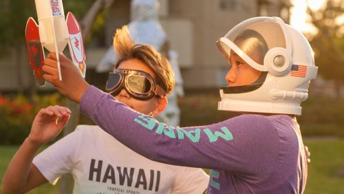 Free Two kids engage in imaginative play with astronaut gear and rocket toy outdoors. Stock Photo