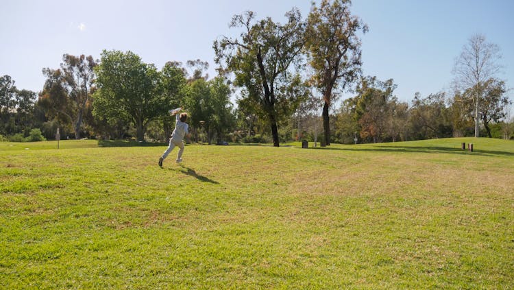 A Person Running On Green Grass Field