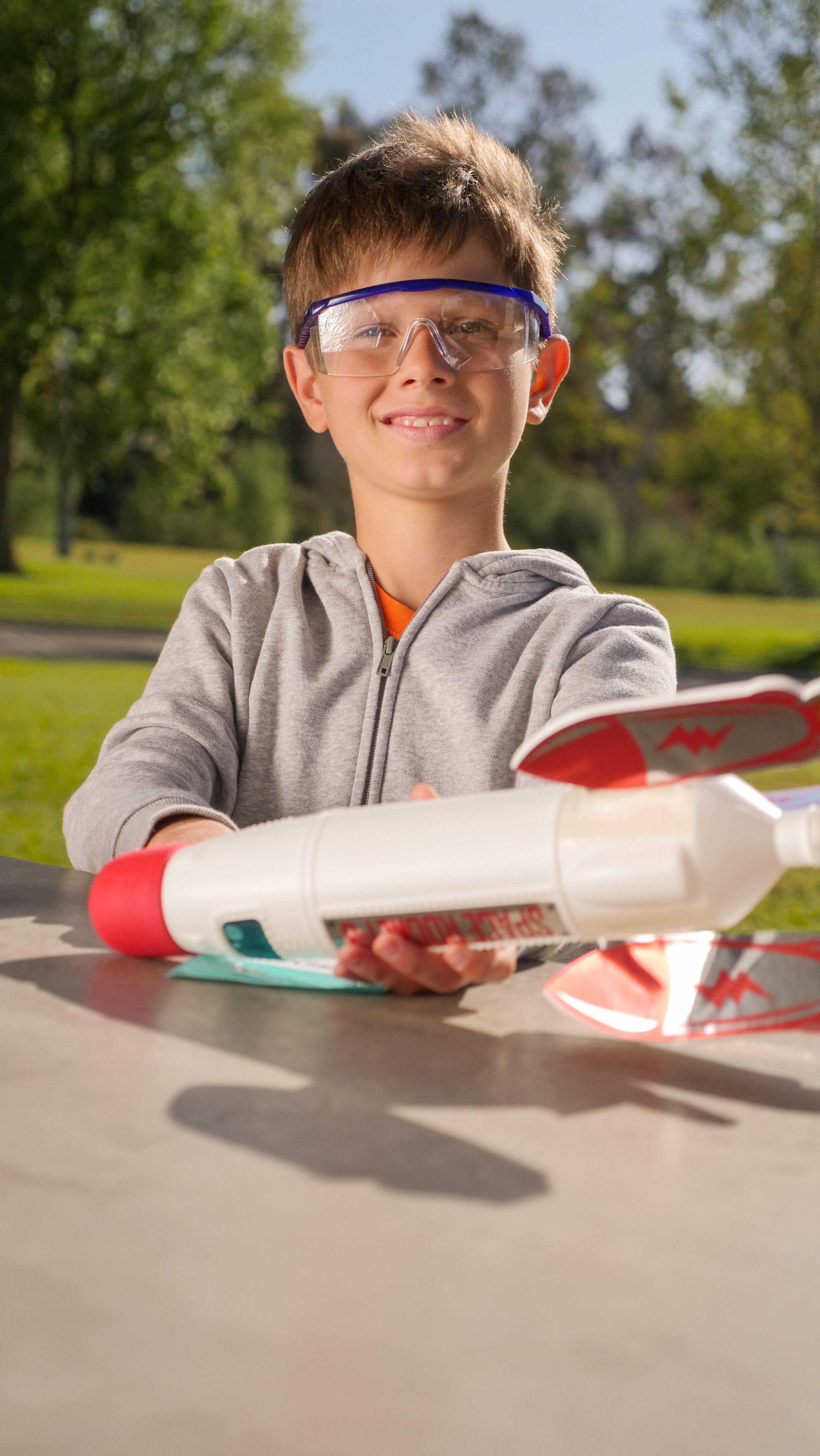 Boy in protective goggles holding a toy rocket outdoors, smiling and enjoying playtime.