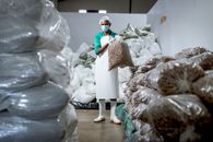 A worker in a face mask and apron organizes stacks of industrial plastic bags in a warehouse.