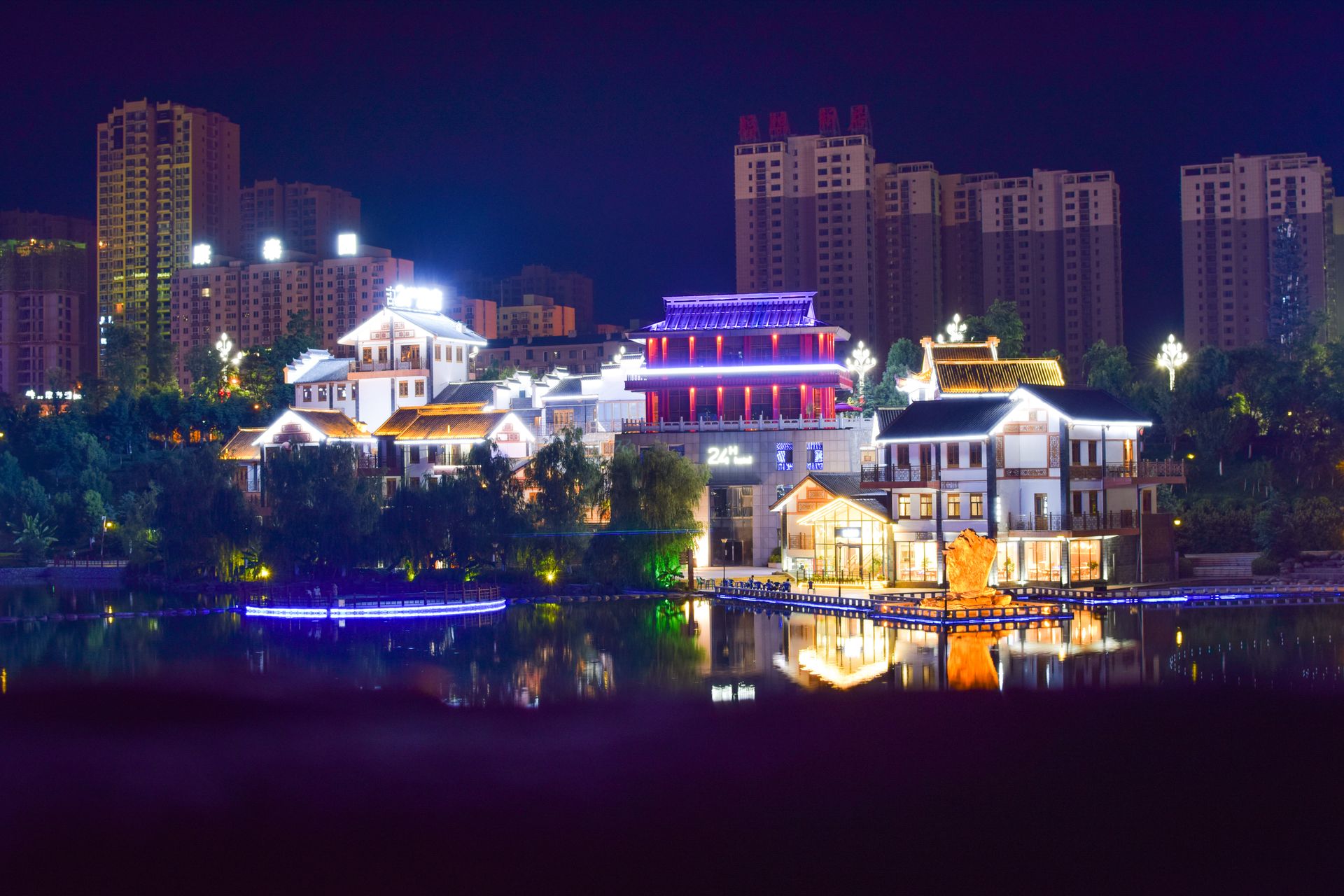 Colorful cityscape with illuminated buildings reflecting on a river at night.